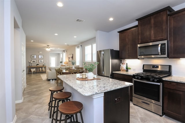 kitchen with a kitchen island, a breakfast bar area, tasteful backsplash, appliances with stainless steel finishes, and ceiling fan