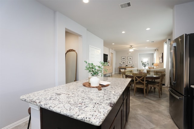 kitchen with stainless steel fridge, a center island, light stone counters, and ceiling fan