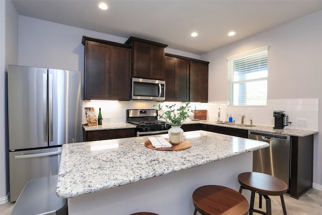 kitchen featuring light stone countertops, appliances with stainless steel finishes, backsplash, a center island, and dark brown cabinetry