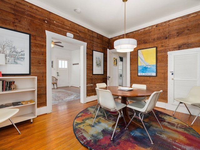 dining space with wood walls, crown molding, hardwood / wood-style flooring, and ceiling fan