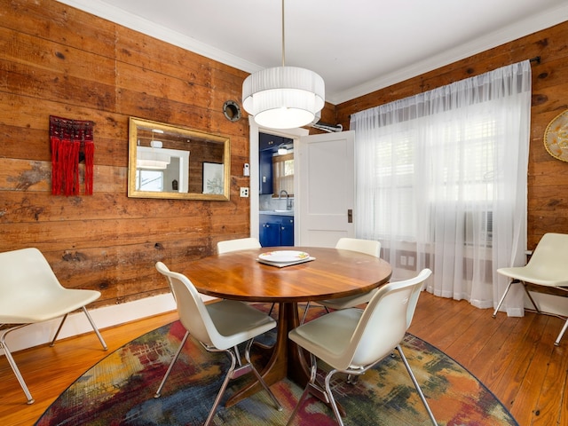 dining space featuring ornamental molding, hardwood / wood-style floors, wooden walls, and sink