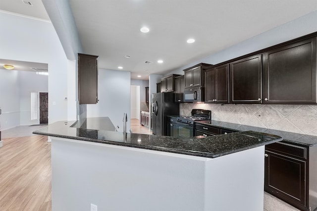 kitchen featuring light wood-type flooring, tasteful backsplash, dark stone counters, black gas range oven, and stainless steel fridge with ice dispenser