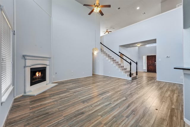 unfurnished living room with ceiling fan, a towering ceiling, and dark wood-type flooring