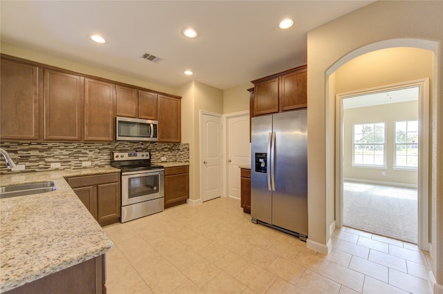 kitchen featuring stainless steel appliances, light stone counters, decorative backsplash, light carpet, and sink