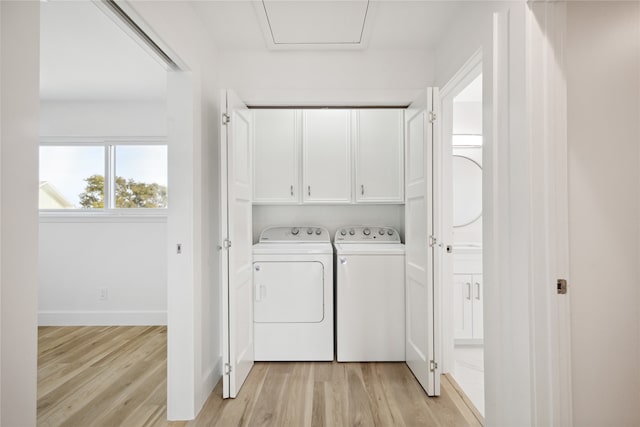 clothes washing area with cabinets, washing machine and dryer, and light wood-type flooring