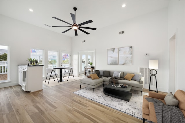 living room featuring a towering ceiling, light hardwood / wood-style flooring, sink, and ceiling fan