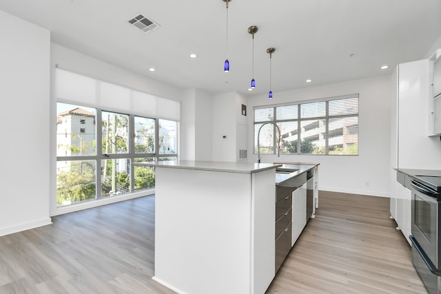 kitchen featuring white cabinets, a center island with sink, stainless steel range with electric stovetop, decorative light fixtures, and light hardwood / wood-style floors