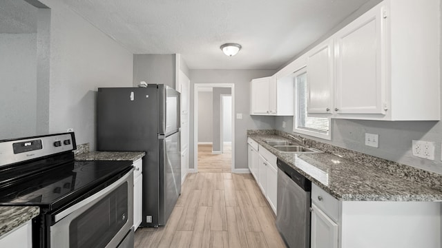 kitchen with appliances with stainless steel finishes, sink, light wood-type flooring, white cabinetry, and dark stone counters