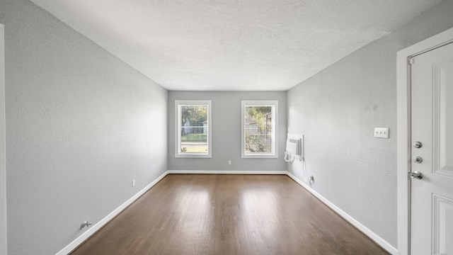 unfurnished room with a textured ceiling, dark hardwood / wood-style flooring, and a wall mounted air conditioner