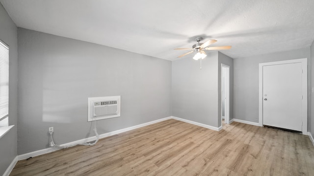 spare room with a wall mounted air conditioner, light wood-type flooring, and ceiling fan