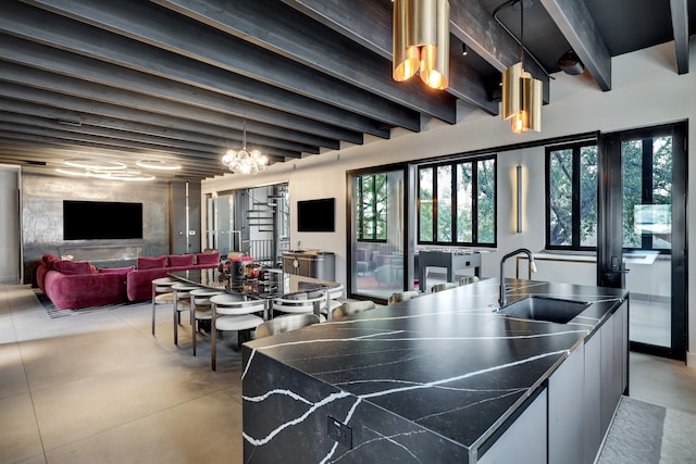 kitchen featuring a kitchen island with sink, beam ceiling, sink, an inviting chandelier, and white cabinets