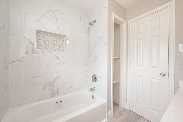 bathroom with wood-type flooring, a textured ceiling, and tiled shower / bath