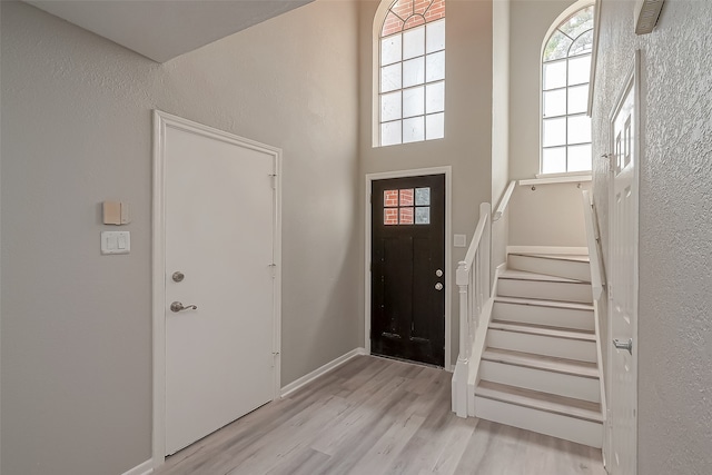 foyer entrance with a towering ceiling and light wood-type flooring