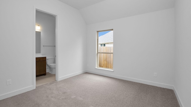 unfurnished bedroom with lofted ceiling, ensuite bathroom, and light carpet