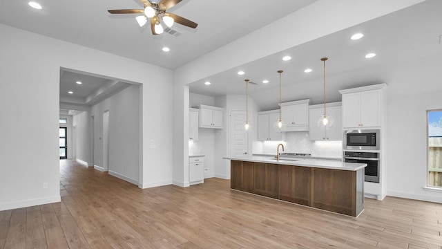 kitchen with built in microwave, sink, an island with sink, oven, and white cabinets