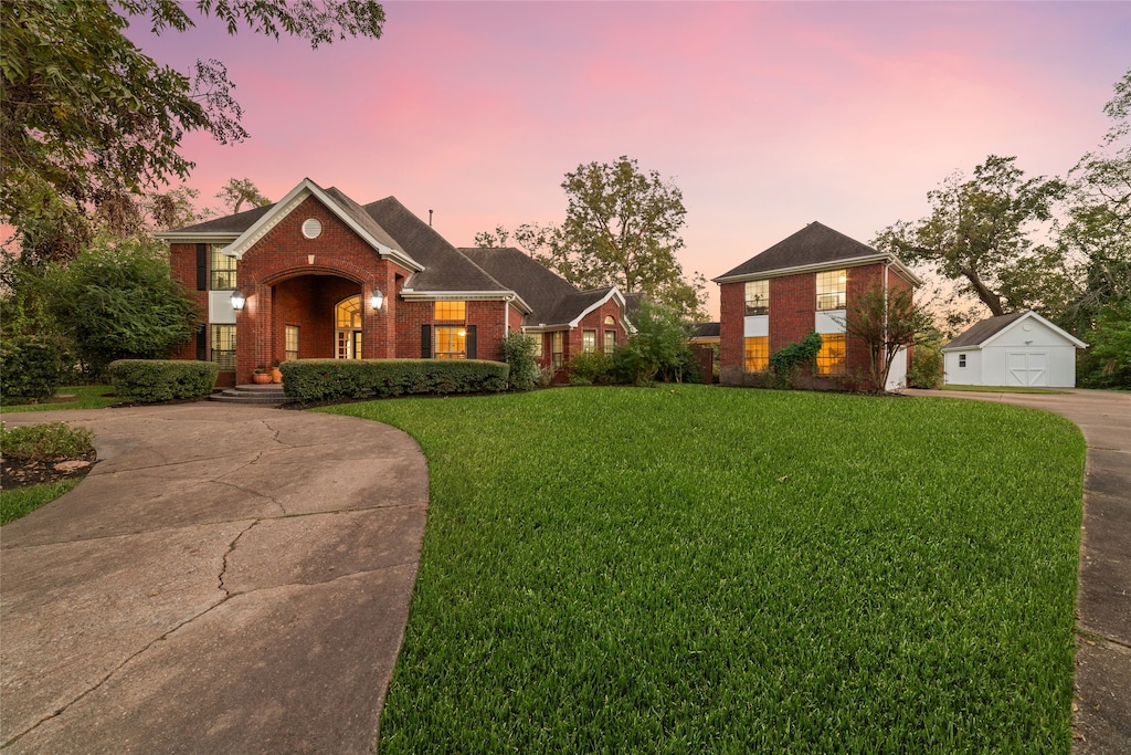 view of front of home featuring driveway, a front yard, an outdoor structure, and brick siding