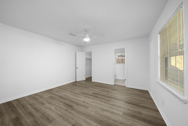 unfurnished bedroom featuring a spacious closet, ceiling fan, a closet, and hardwood / wood-style floors