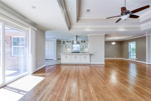 unfurnished living room featuring ceiling fan, a tray ceiling, ornamental molding, and light hardwood / wood-style flooring