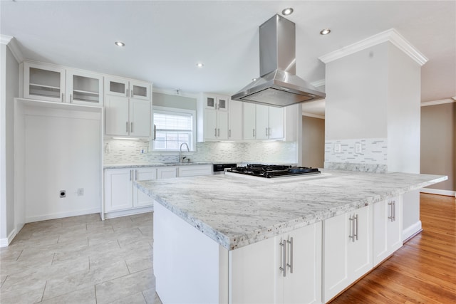 kitchen featuring wall chimney range hood, stainless steel gas cooktop, light stone counters, white cabinets, and crown molding