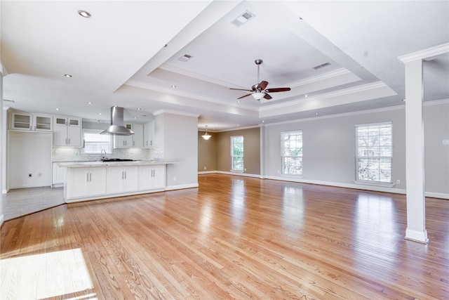 unfurnished living room featuring sink, light wood-type flooring, a tray ceiling, ceiling fan, and ornamental molding