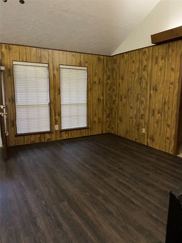 spare room with a textured ceiling, wooden walls, dark wood-type flooring, and vaulted ceiling