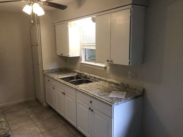 kitchen featuring white cabinets, ceiling fan, light tile patterned floors, stone countertops, and sink