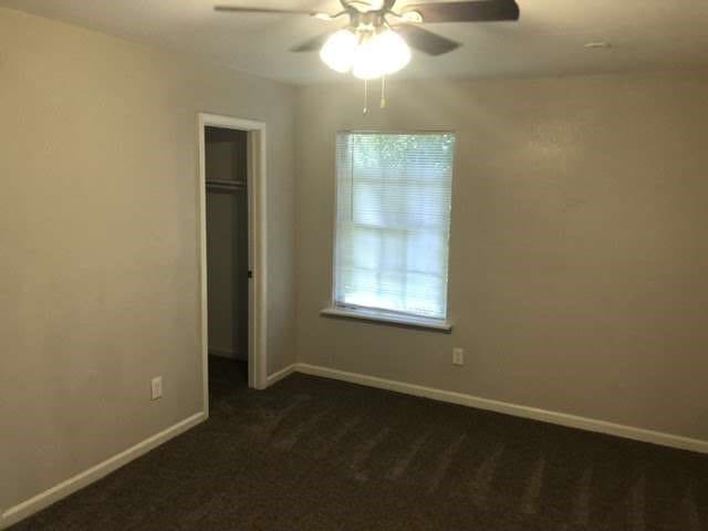 unfurnished bedroom featuring dark colored carpet, a closet, and ceiling fan