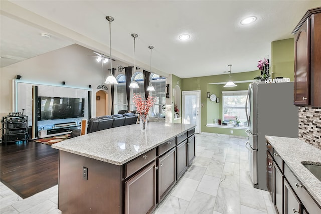 kitchen with decorative light fixtures, decorative backsplash, dark brown cabinets, light stone countertops, and a kitchen island