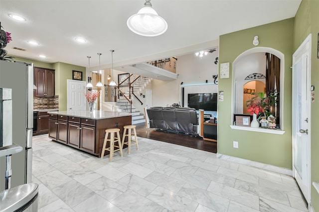 kitchen featuring a center island, decorative light fixtures, a kitchen bar, decorative backsplash, and dark brown cabinetry