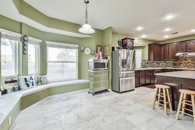 kitchen featuring stainless steel appliances, a kitchen bar, tasteful backsplash, dark brown cabinetry, and pendant lighting