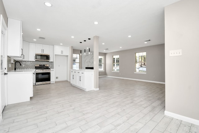 kitchen with white cabinetry, light hardwood / wood-style floors, stainless steel appliances, pendant lighting, and decorative backsplash