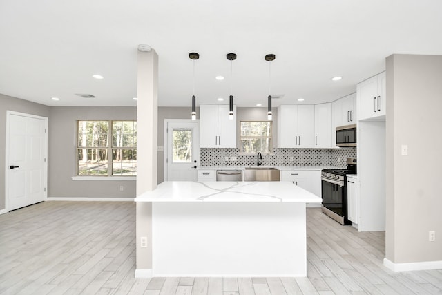 kitchen with a kitchen island, appliances with stainless steel finishes, decorative light fixtures, and white cabinets