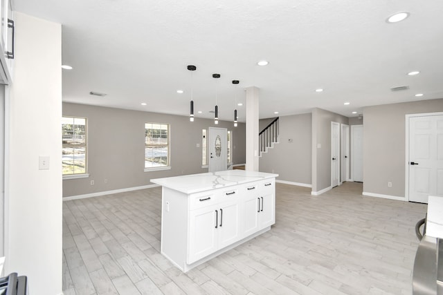 kitchen featuring white cabinets, hanging light fixtures, a kitchen island, light hardwood / wood-style floors, and light stone counters