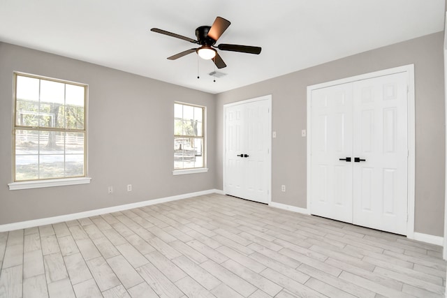 unfurnished bedroom featuring ceiling fan, multiple windows, light wood-type flooring, and two closets