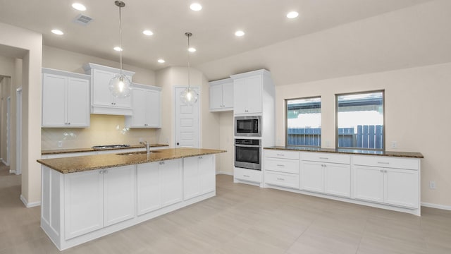 kitchen featuring white cabinetry, dark stone counters, hanging light fixtures, a kitchen island with sink, and stainless steel appliances