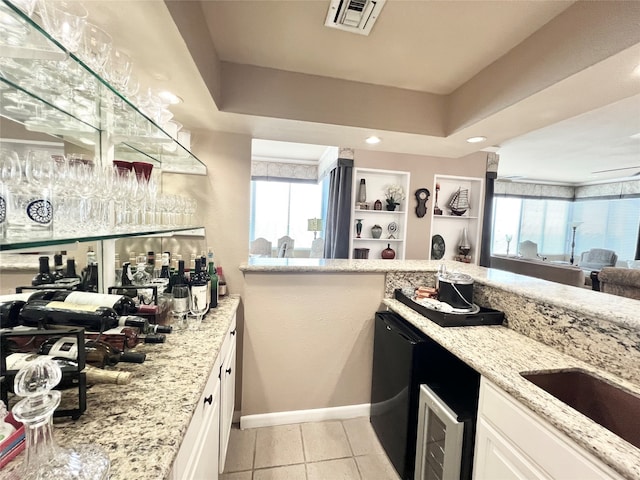 kitchen with a raised ceiling, light tile patterned floors, white cabinetry, light stone countertops, and dishwasher