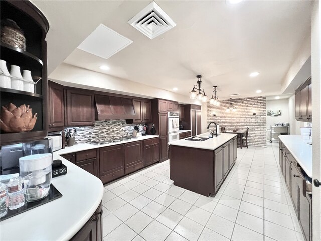 kitchen featuring a kitchen island with sink, sink, light tile patterned flooring, decorative light fixtures, and premium range hood