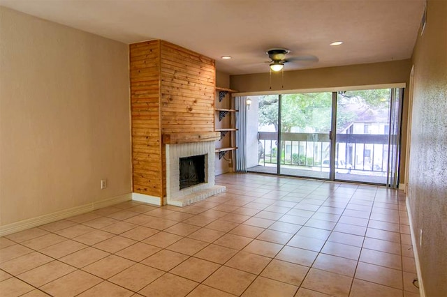 unfurnished living room featuring ceiling fan, wood walls, light tile patterned floors, and a brick fireplace