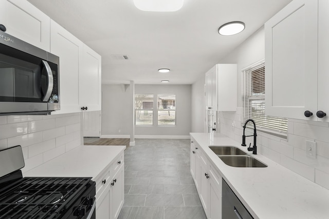 kitchen with black range oven, sink, white cabinets, and backsplash