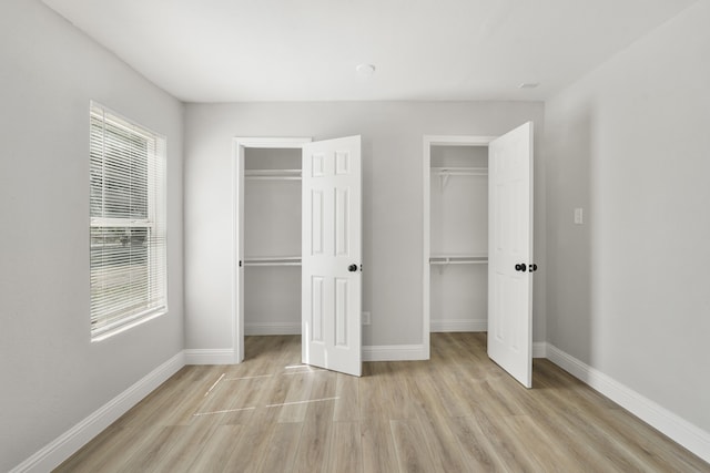 unfurnished bedroom with multiple closets and light hardwood / wood-style floors