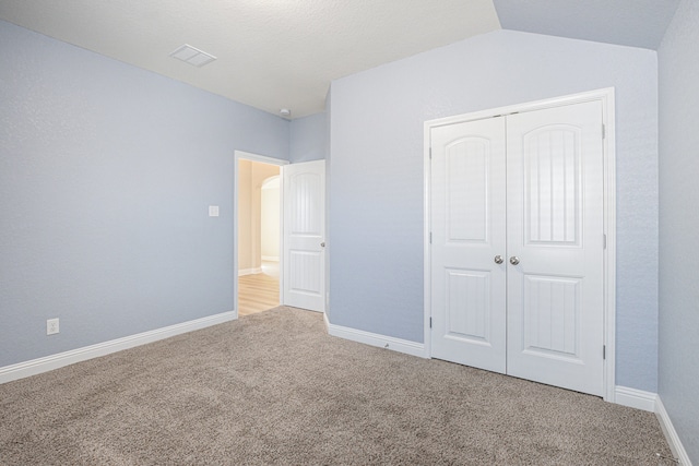 unfurnished bedroom featuring light carpet, a closet, and lofted ceiling