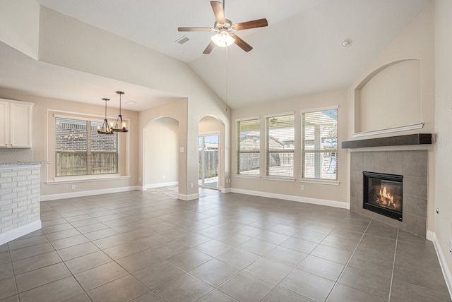 unfurnished living room with a tiled fireplace, tile patterned floors, lofted ceiling, and ceiling fan with notable chandelier