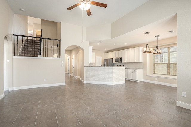 unfurnished living room with dark tile patterned flooring, a towering ceiling, and ceiling fan with notable chandelier