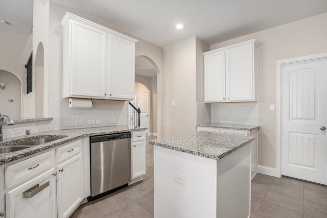 kitchen featuring a kitchen island, white cabinetry, dishwasher, sink, and light stone counters