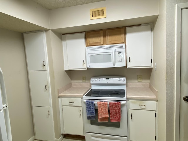 kitchen with white appliances, a textured ceiling, and white cabinets