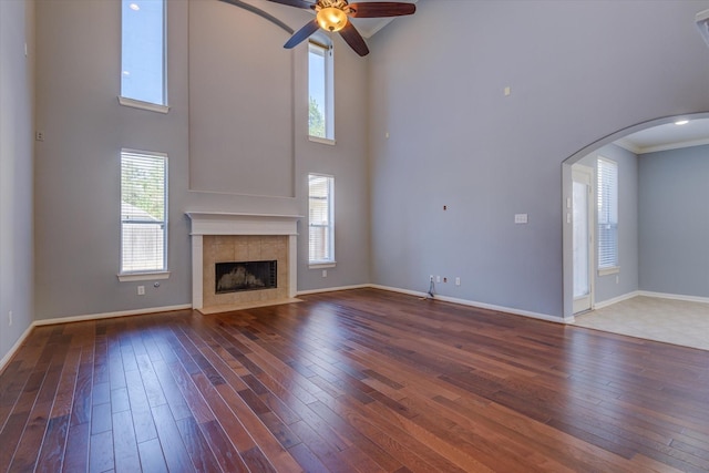 17519 Bighorn River Ln, Humble, TX 77346 - unfurnished living room with arched walkways, hardwood / wood-style flooring, a towering ceiling, ceiling fan, and a tiled fireplace