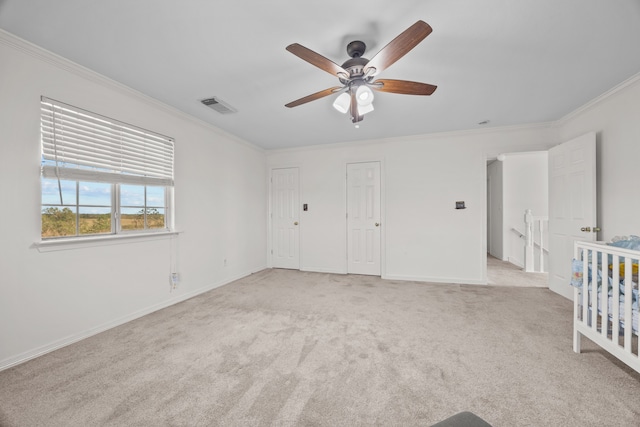 unfurnished bedroom featuring a crib, a closet, crown molding, light colored carpet, and ceiling fan