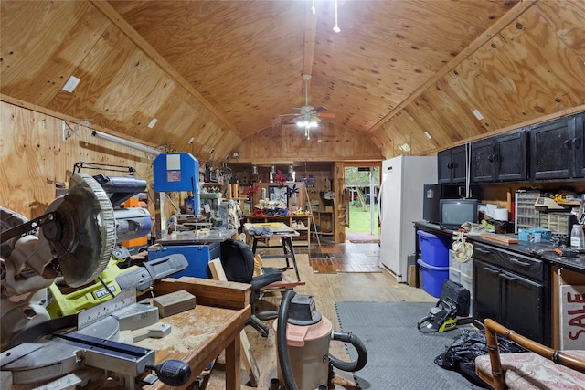 misc room featuring ceiling fan, vaulted ceiling, wood walls, light hardwood / wood-style floors, and a workshop area