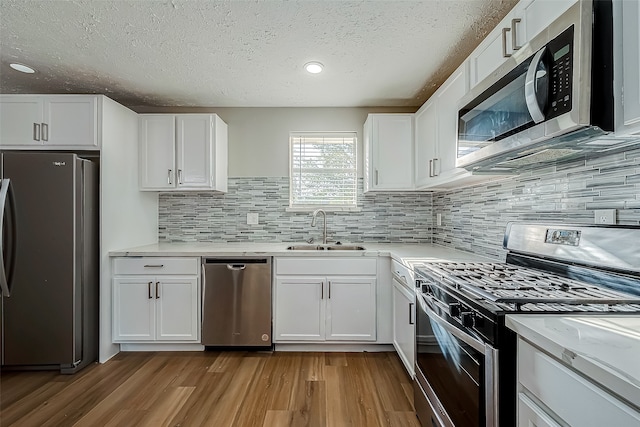 kitchen featuring white cabinets, tasteful backsplash, appliances with stainless steel finishes, light wood-type flooring, and sink