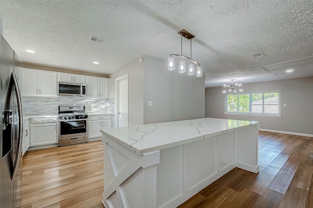 kitchen with appliances with stainless steel finishes, light hardwood / wood-style flooring, white cabinetry, and hanging light fixtures